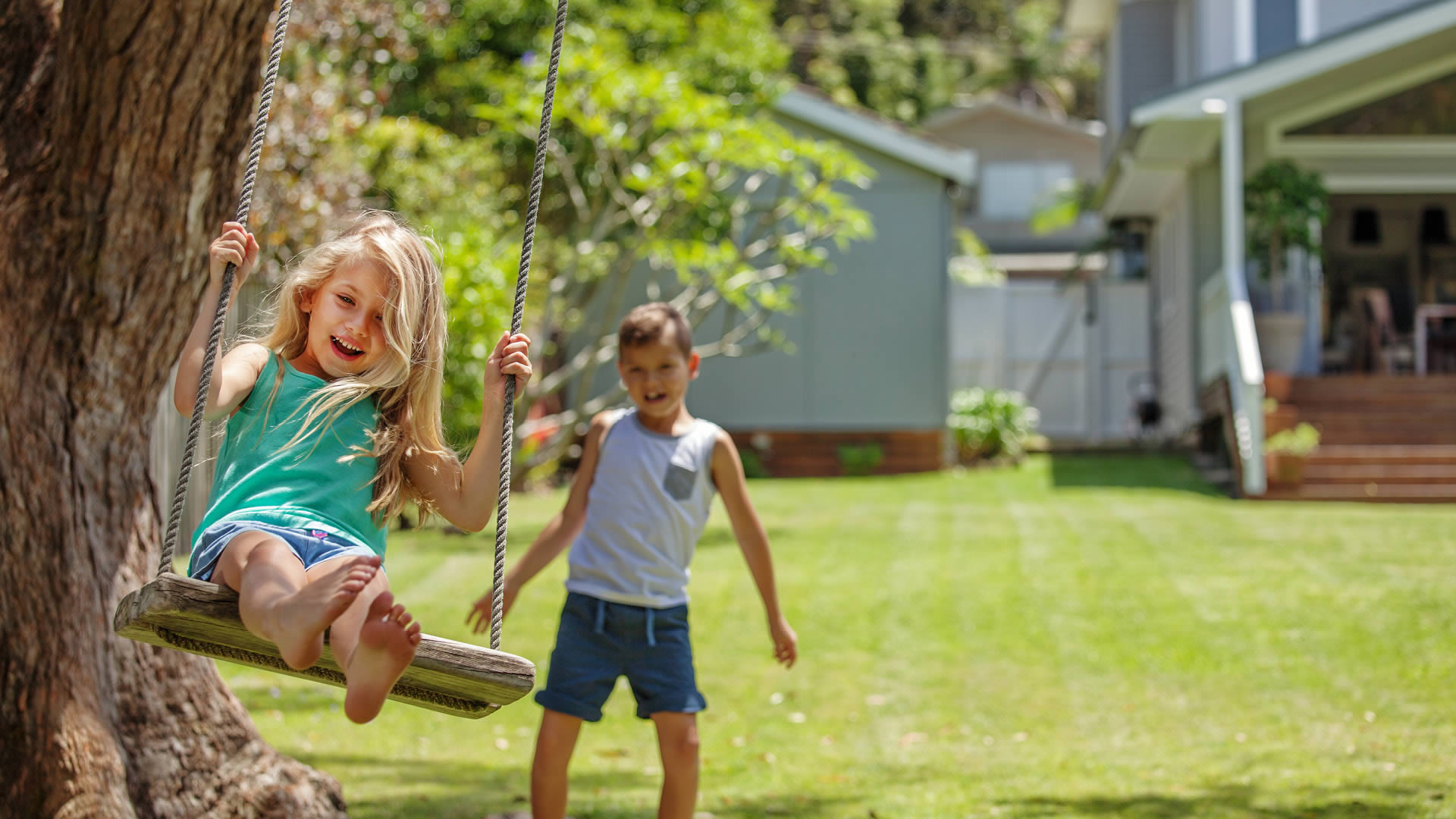 На летних каникулах на даче. Дети на качелях. Дети на качелях во дворе. Дети играют во дворе. Семья на качелях.